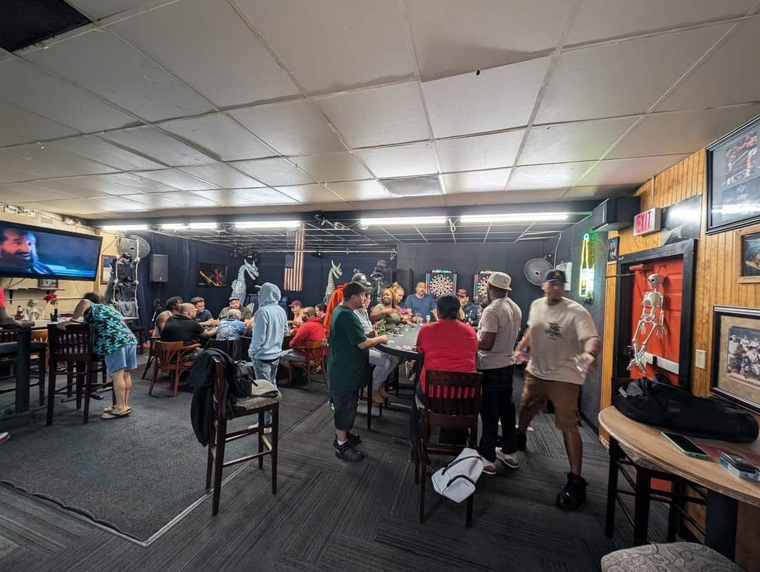 Busy indoor bar with people chatting and dancing under bright lights and a hanging TV