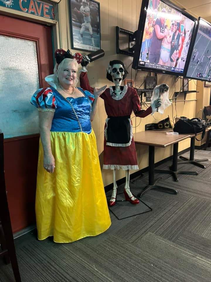 Two Halloween-costumed figures stand by a doorway in an indoor hall, one in blue and yellow, one in red and black.