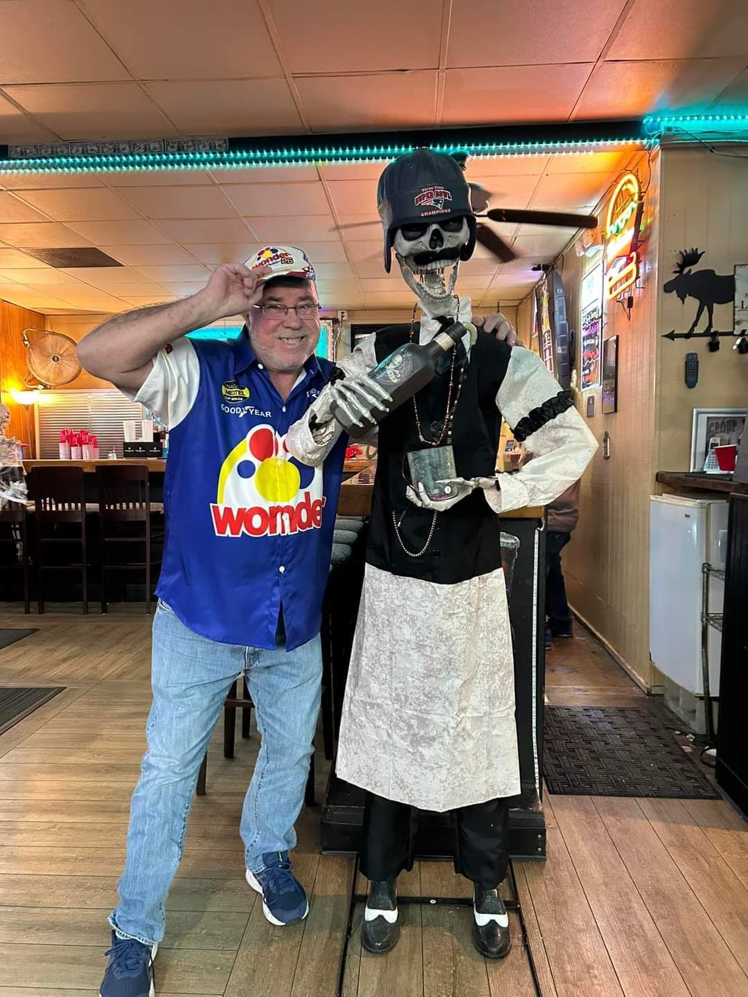 Man poses beside a life-size skeleton in a restaurant hallway, both facing the camera.