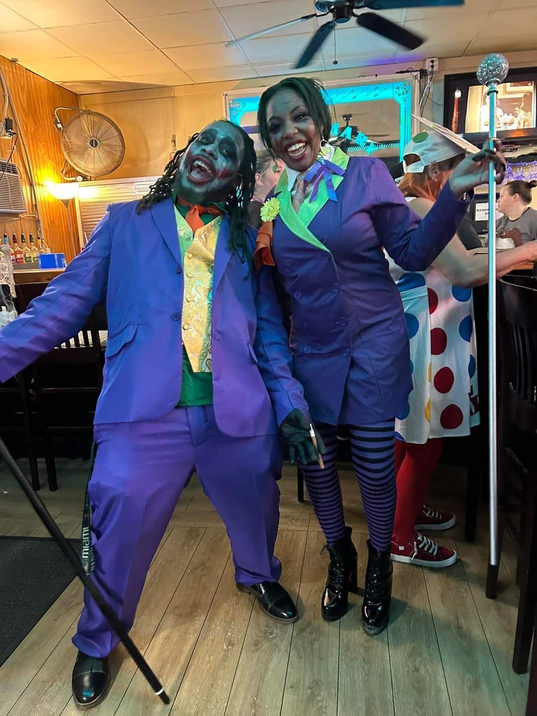 Two people in purple suits and neon ties pose indoors, smiling and holding canes.