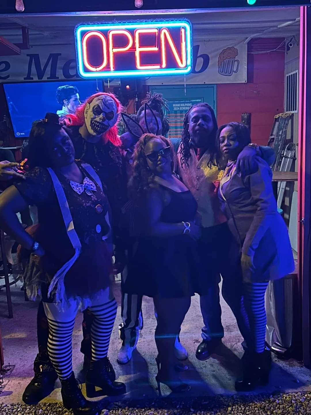 Group of people posing outside a shop under a neon “OPEN” sign at night.