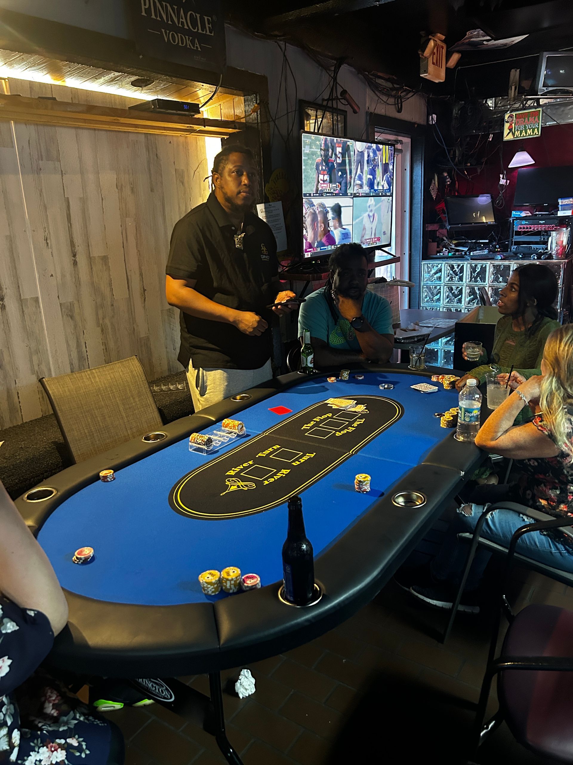People playing cards at a blue poker table in a dim bar lounge