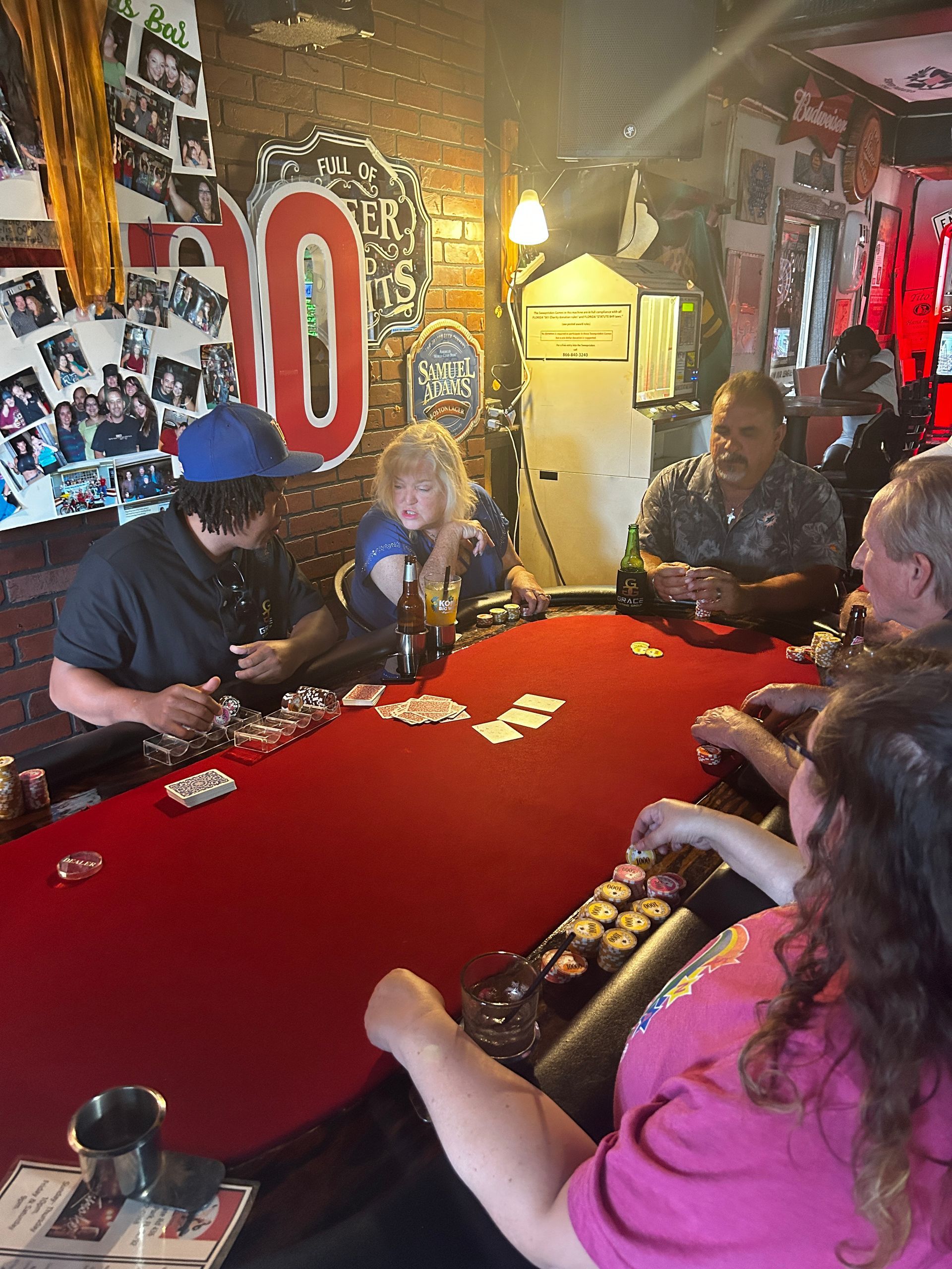 People playing cards around a red table in a cozy, cluttered bar with warm lighting