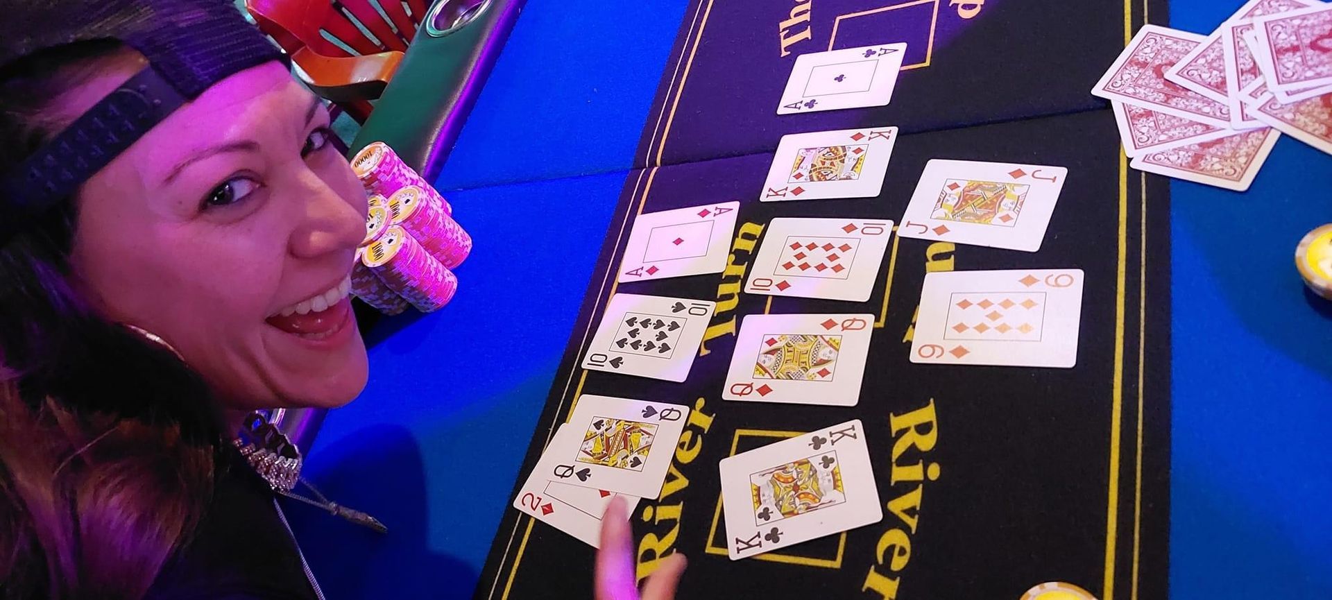 Woman smiling beside a table of playing cards at a brightly lit game table.