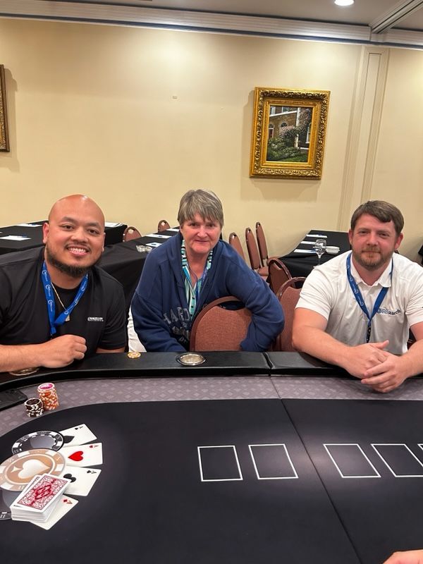 Three people seated at a casino table, smiling, with chips and cards in front of them.