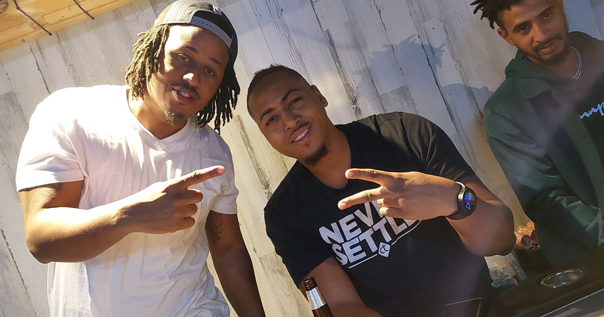 Three people posing outdoors, smiling and making hand gestures in casual clothes.