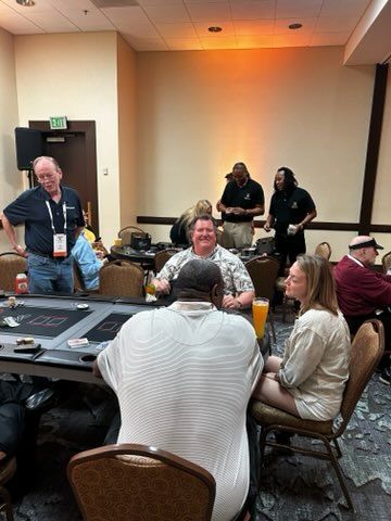 People seated around tables in a conference room, chatting during a meeting or workshop.