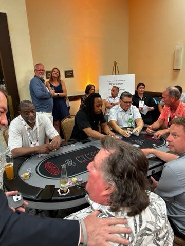 People gathered around a casino-style card table in a conference room, watching and chatting.