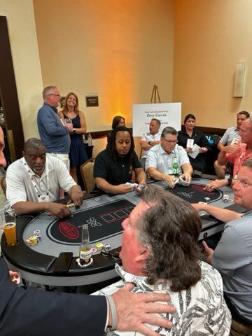 People gathered around a blackjack table in a warmly lit casino room, with a dealer and spectators watching.