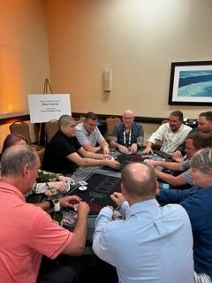 Group of people seated in a conference room, playing a card game around a table.