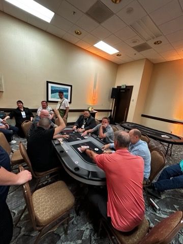 People gathered around a casino table in a conference room, talking and playing cards.