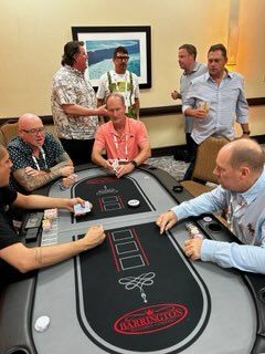 People gathered around a casino table, watching and talking in a hotel room.