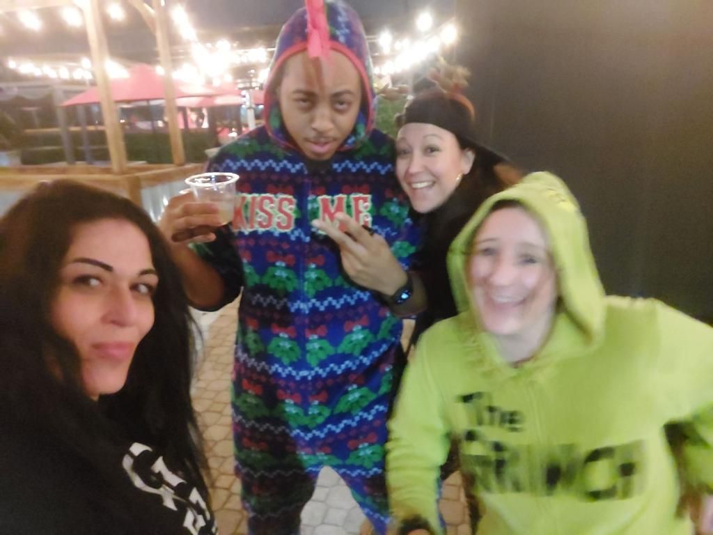 Four people smiling at a nightclub, one holding a drink and wearing bright hoodies.