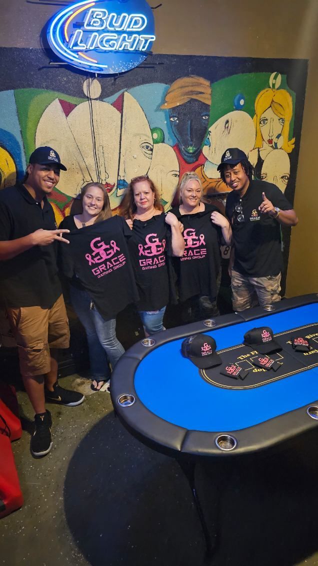 Group posing beside a blue casino table with drinks, Bud Light sign, and colorful mural background