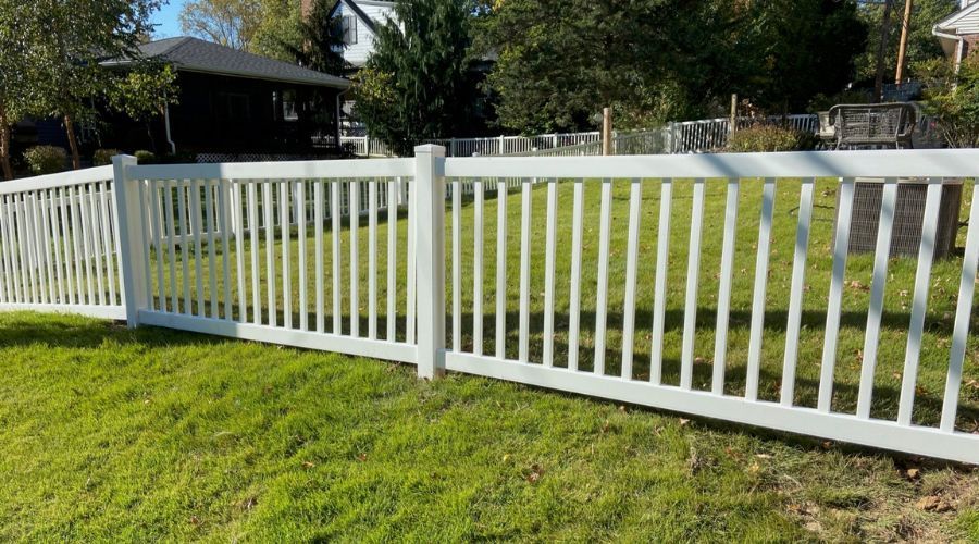 White vinyl picket fence in a residential backyard, illustrating factors affecting fence lifespan in
