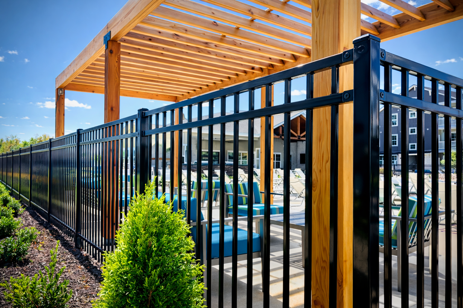 A black metal fence surrounds a sunny patio area with a wooden pergola and outdoor furniture.