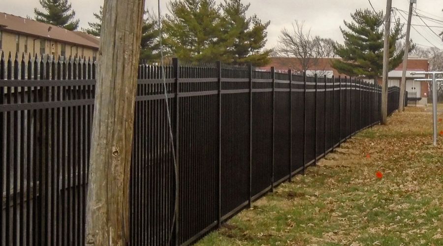 A long black metal security fence with pointed spear-top pickets installed along a property line in