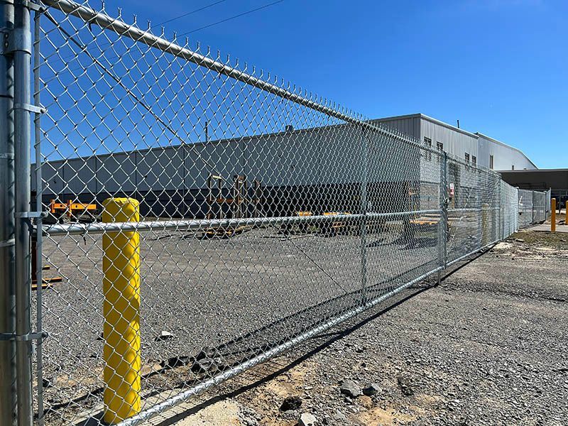 A chain link fence with a yellow pole in front of a large building.