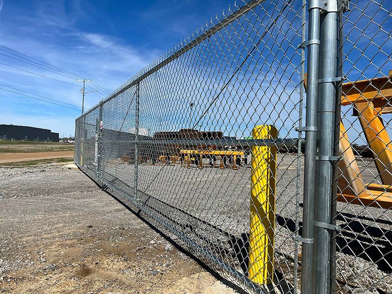 A chain link fence with a yellow post in front of a building.