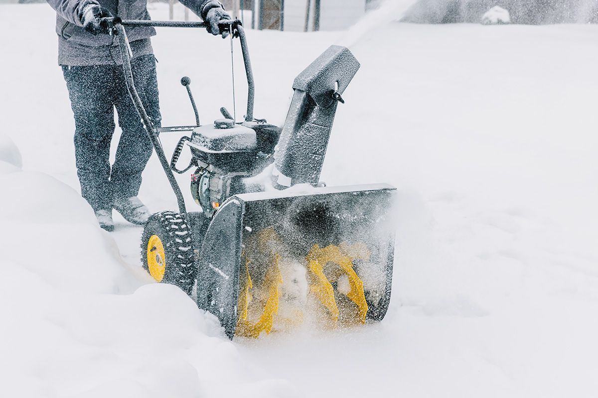 A man is using a snow blower to clear snow from his driveway.