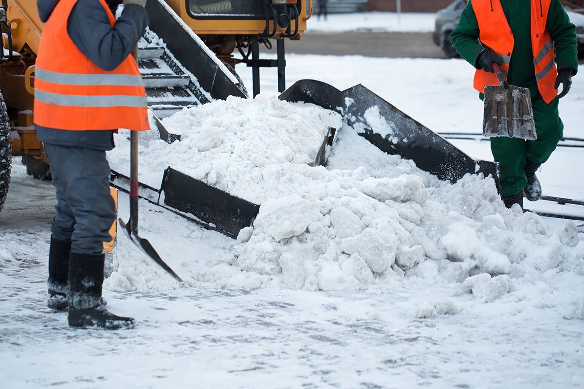 Two men are shoveling snow in a parking lot.