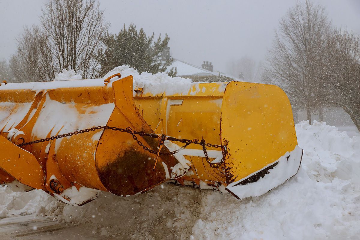 A yellow snow plow is parked in the snow on a snowy day.