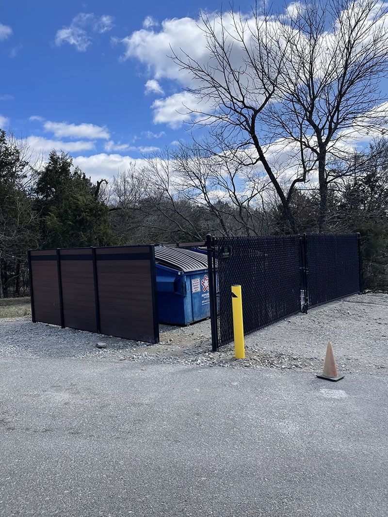A dumpster is behind a fence in a parking lot.