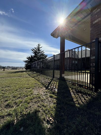 The sun is shining through the fence and casting a shadow on the grass.
