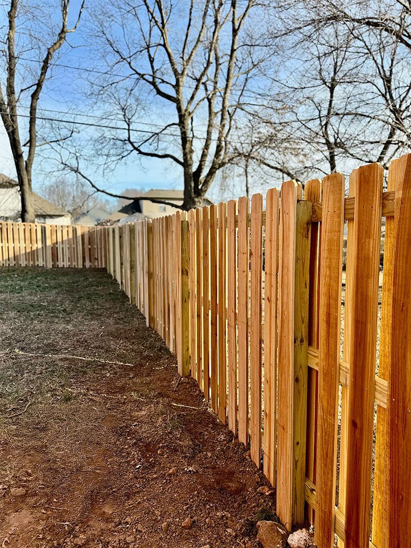 A wooden picket fence surrounds a dirt path in a backyard.