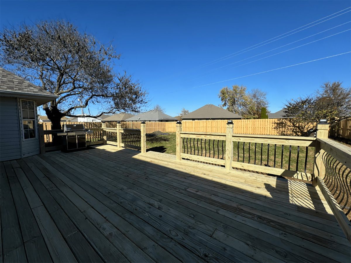 A large wooden deck with a fence and a tree in the background.