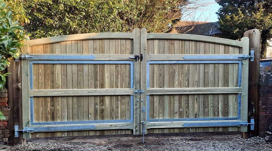 Heavy-duty wooden double driveway gate reinforced with a galvanized steel frame and metal hinges.