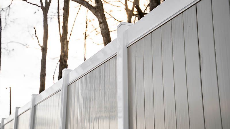 A close up of a white fence with trees in the background.