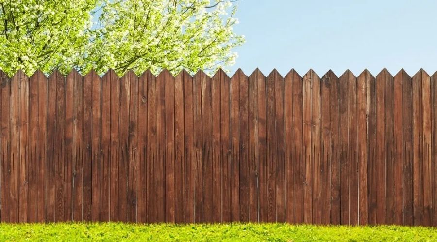 Stained wooden privacy fence with pointed pickets along a green lawn.