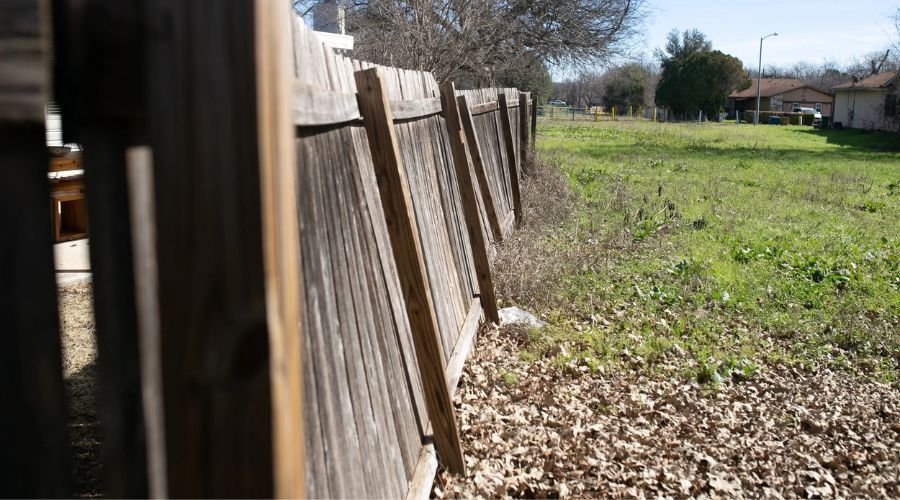 Leaning wooden privacy fence propped up with temporary wooden supports.