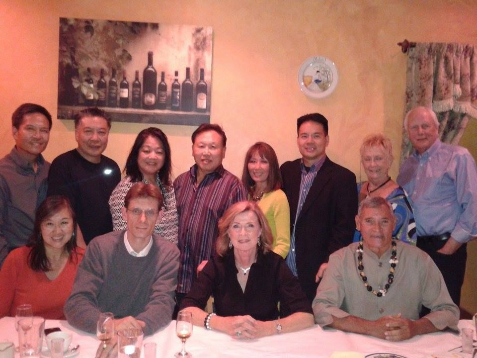 A group of twelve people gathered around a table, posing for a photo in what appears to be a restaurant. 