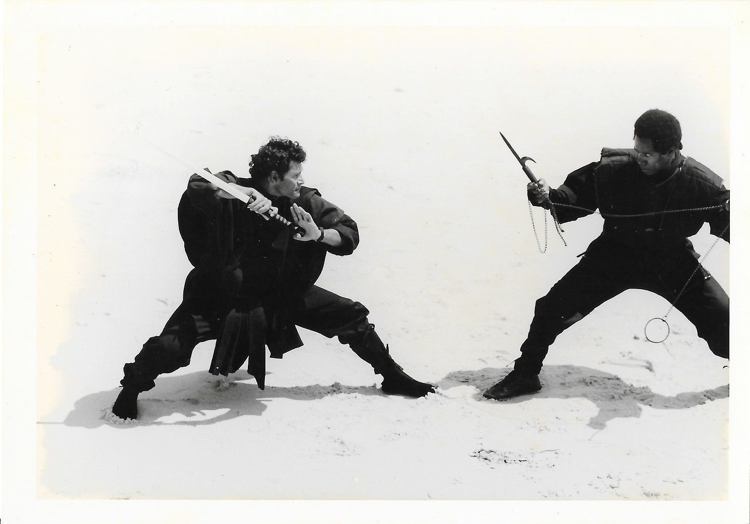 Two men in black clothing engage in a fight outdoors, one with a rifle.