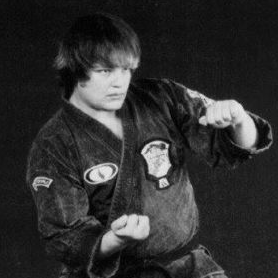 A young man in a martial arts uniform with clenched fists, in a fighting stance. Black and white photo.