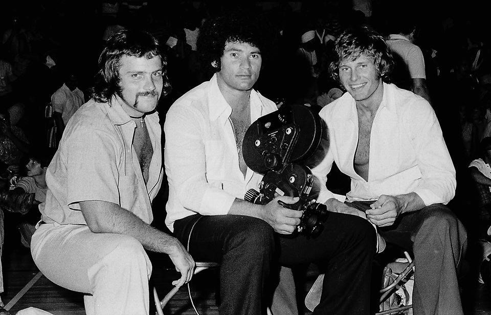 Three men in the 1970s pose for a photo, one holding a trophy.