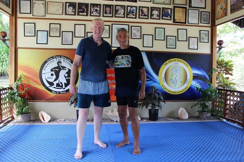 Two men stand together in an outdoor training space, smiling.