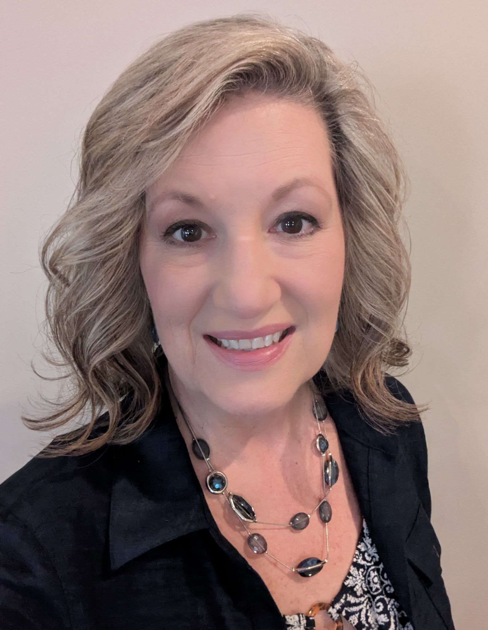 A woman wearing a black jacket and a necklace is smiling for the camera.