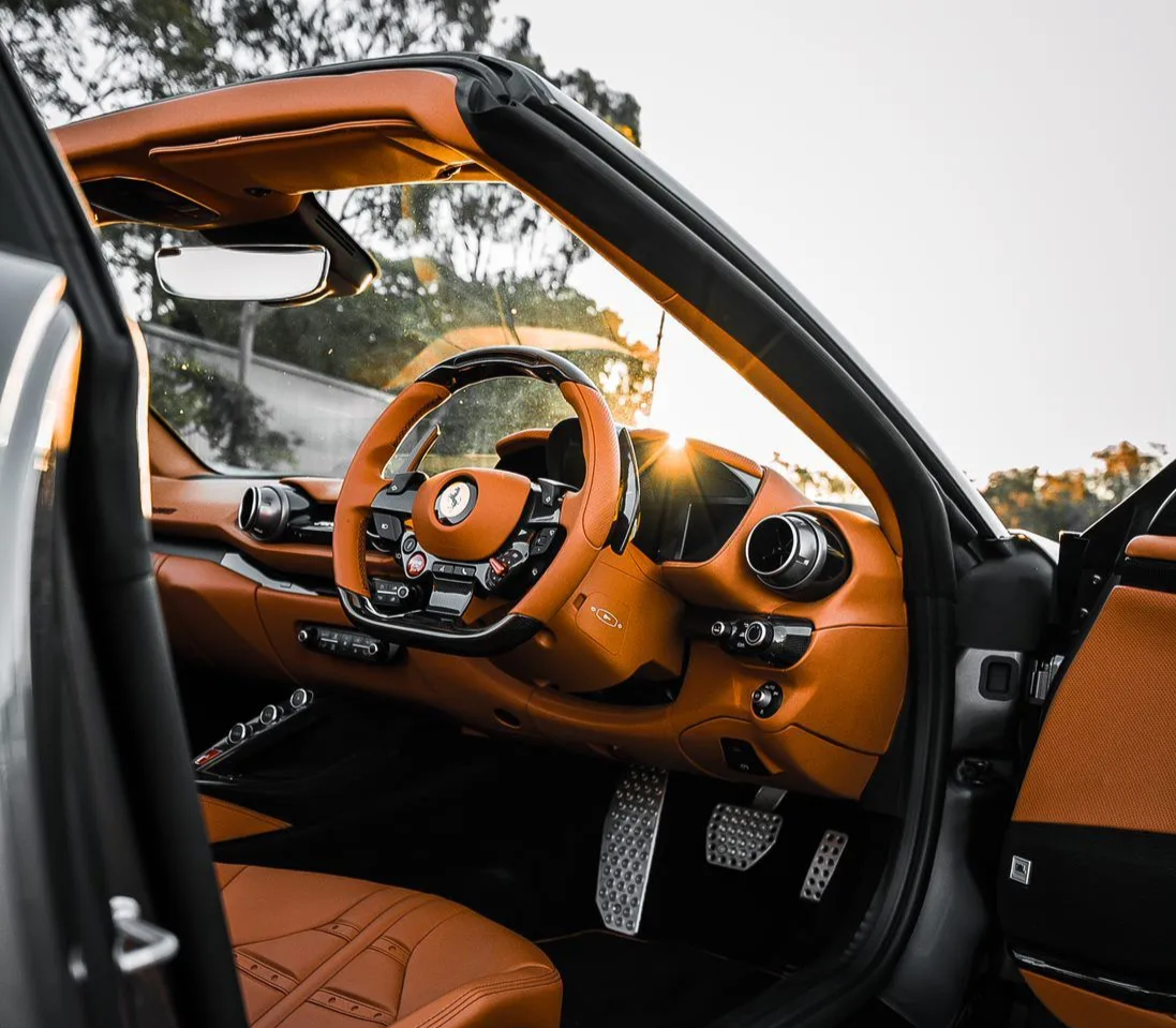 Open car door reveals luxury interior: orange leather seats, steering wheel, and dashboard.