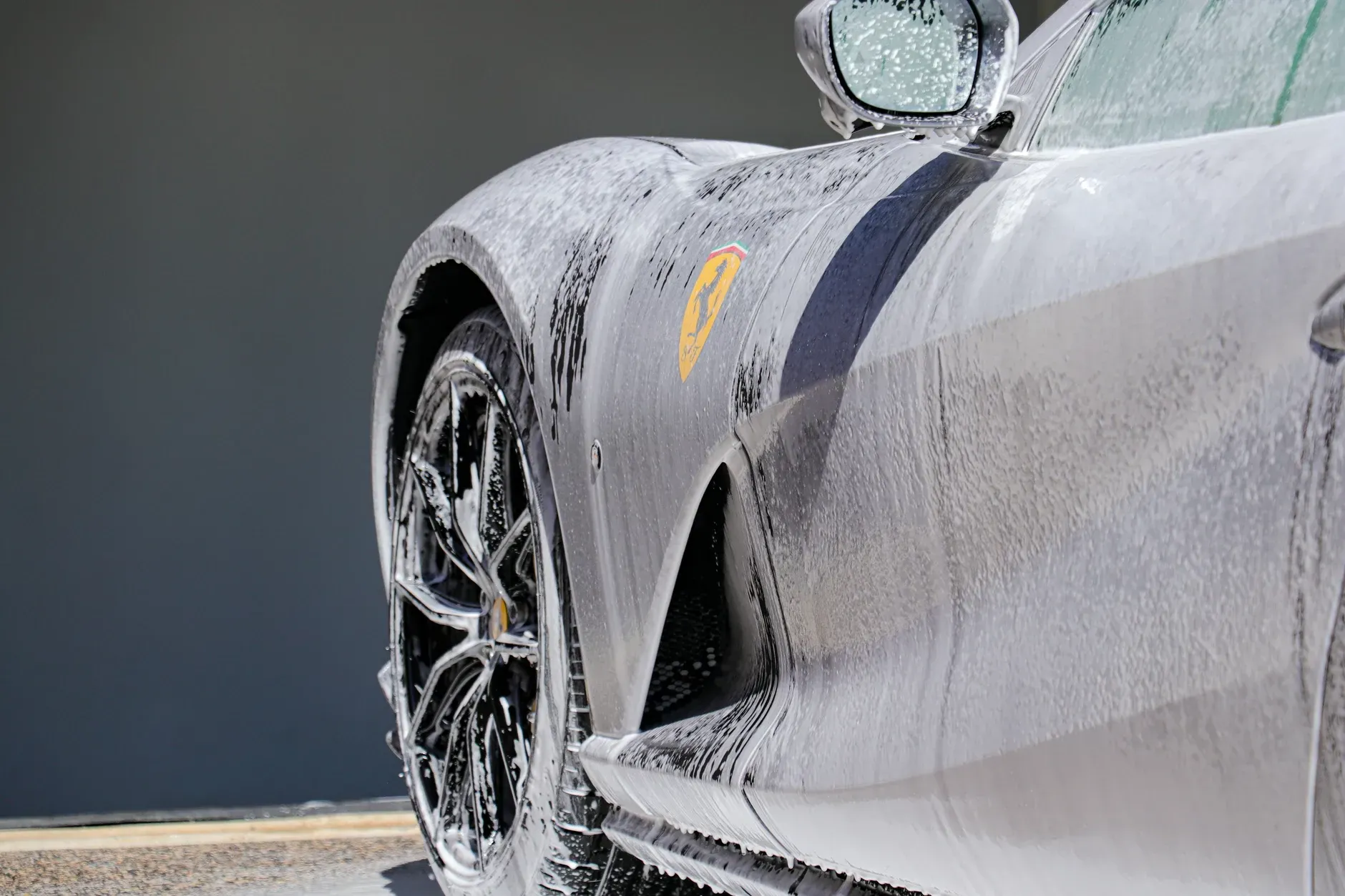 Grey sports car covered in white foam during a car wash.