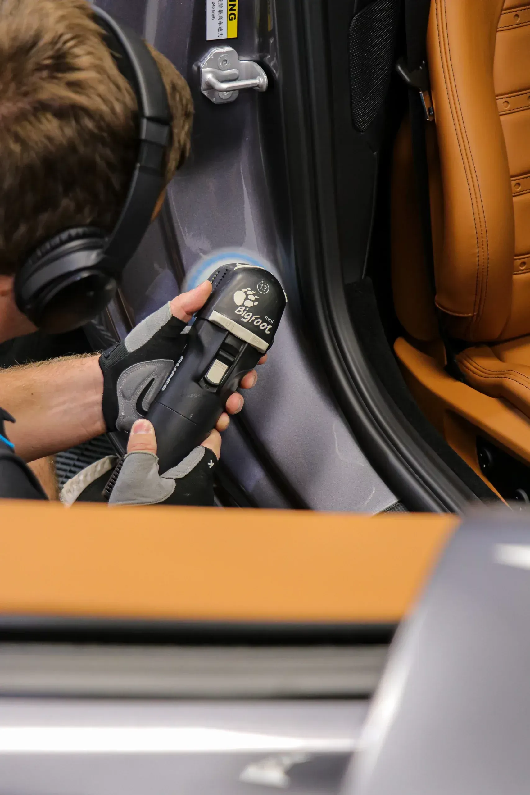 Person using a polisher on a car door panel, near a tan leather seat.