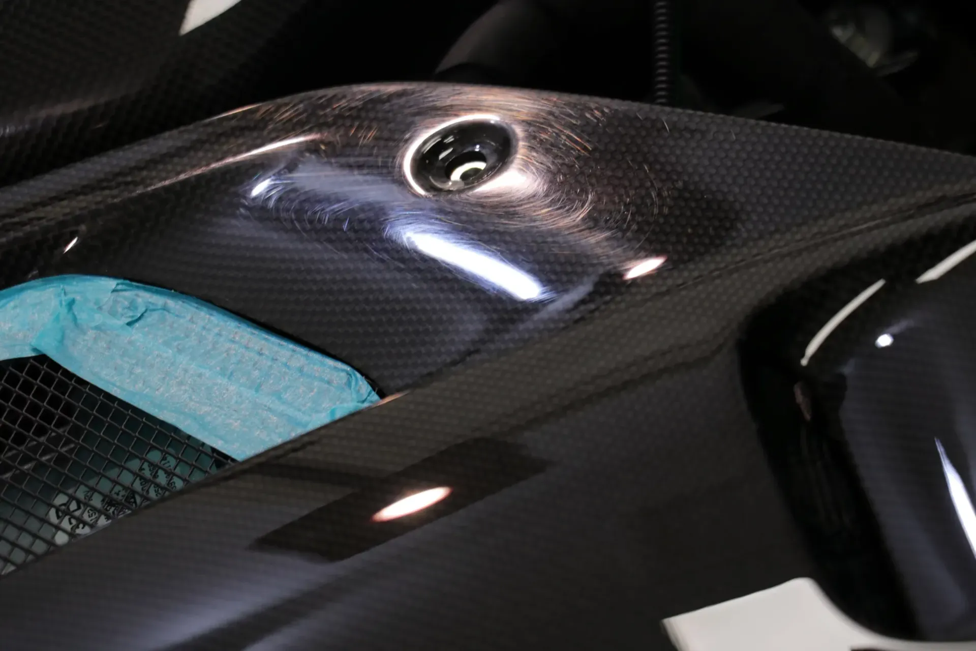 Close-up of a shiny black carbon fiber surface with a hole and a blue sponge peeking out.