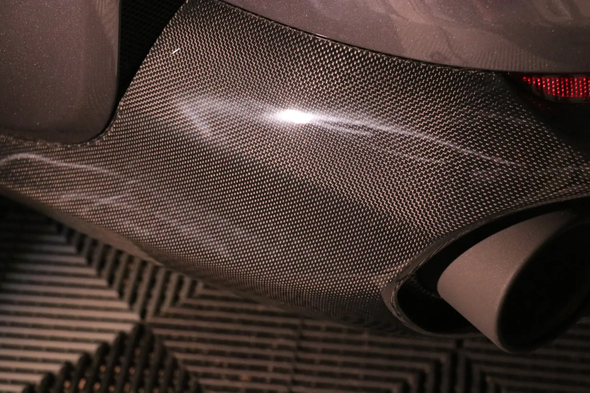 Close-up of a car's exhaust pipe, featuring carbon fiber detailing.