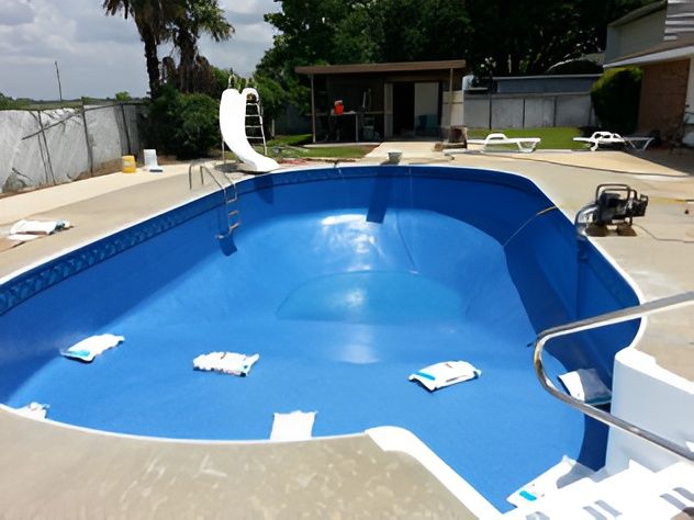 Empty blue pool with white steps and slide, surrounded by concrete.