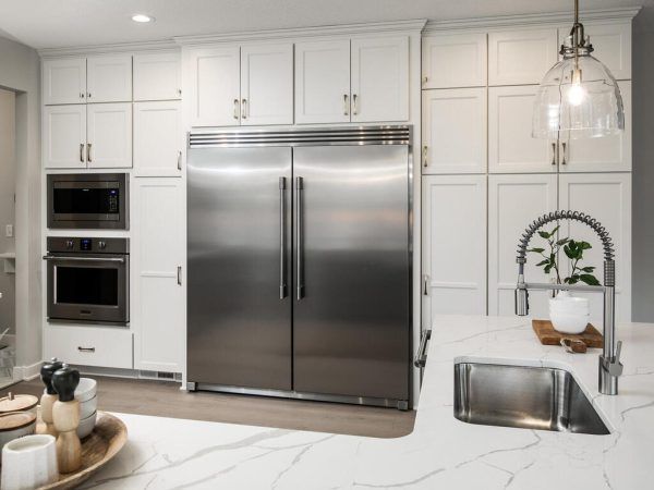 White kitchen with stainless steel refrigerator, oven, and microwave, marble countertops.