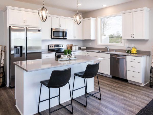 Modern white kitchen with island, stainless steel appliances, and two black bar stools.
