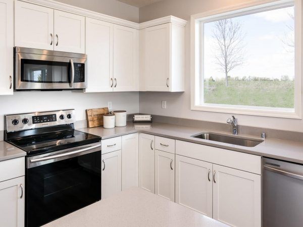 White kitchen with stainless steel appliances, a window overlooking a field.