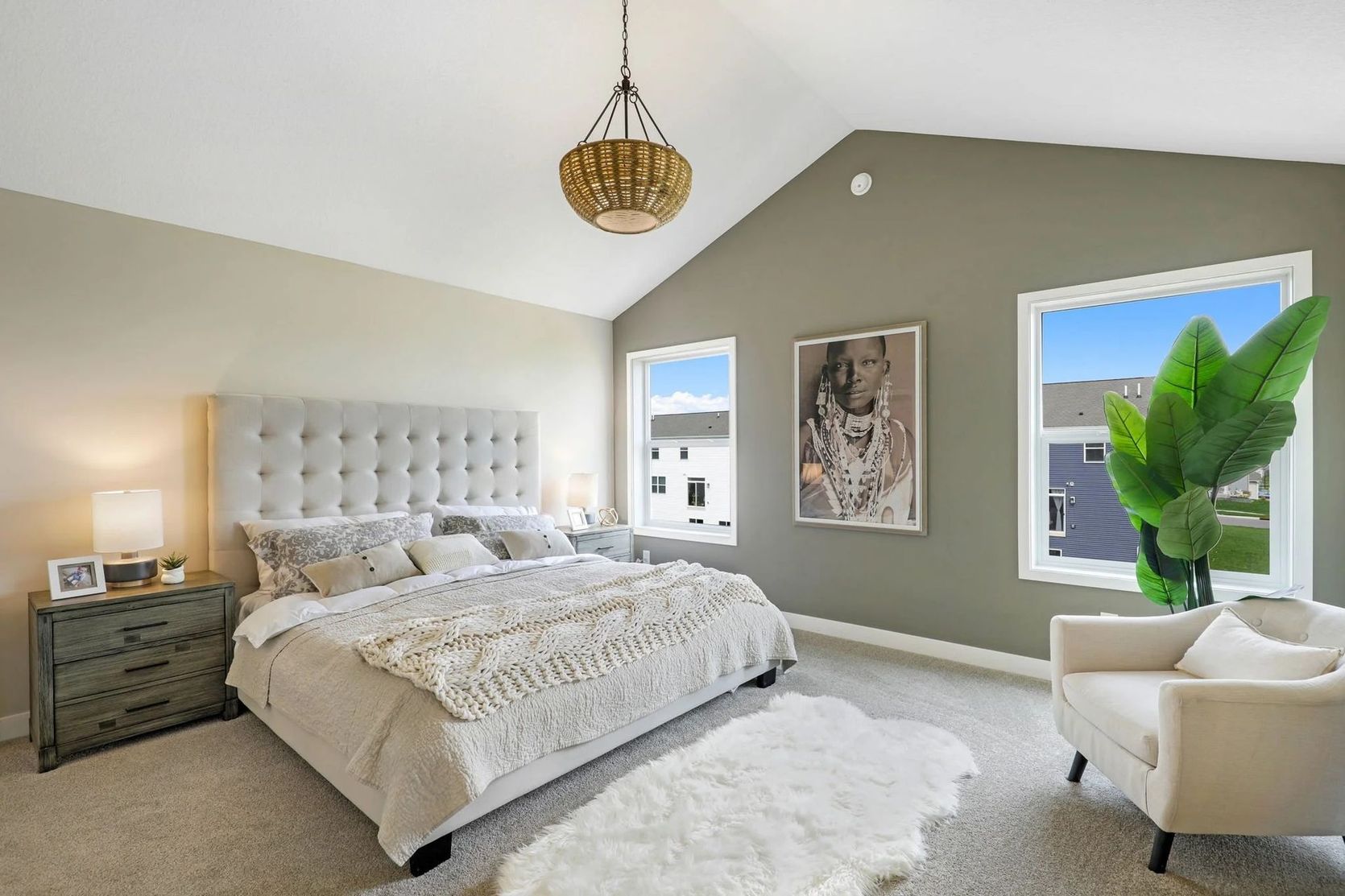 Bedroom with a bed, armchair, two windows, and a decorative hanging light. Neutral tones, carpet flooring.